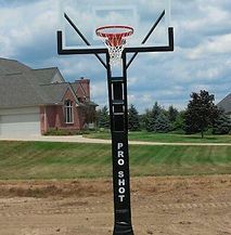 A basketball hoop is sitting on top of a dirt field in front of a house.