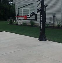 A basketball hoop is sitting on the sidewalk in front of a house.