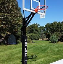 A basketball hoop is sitting in the middle of a lush green field.