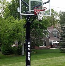 A basketball hoop is sitting in the grass in front of a house.