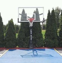 A basketball hoop is sitting on top of a blue basketball court surrounded by trees.