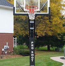 A basketball hoop is sitting in the grass in front of a house.