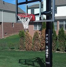 A basketball hoop is sitting in the grass in front of a house.