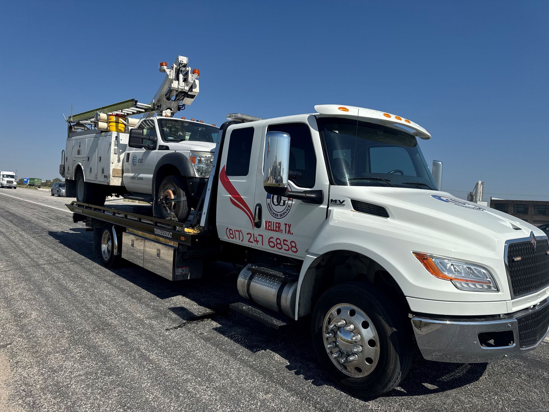 A white truck with a crane on the back is driving down a highway.