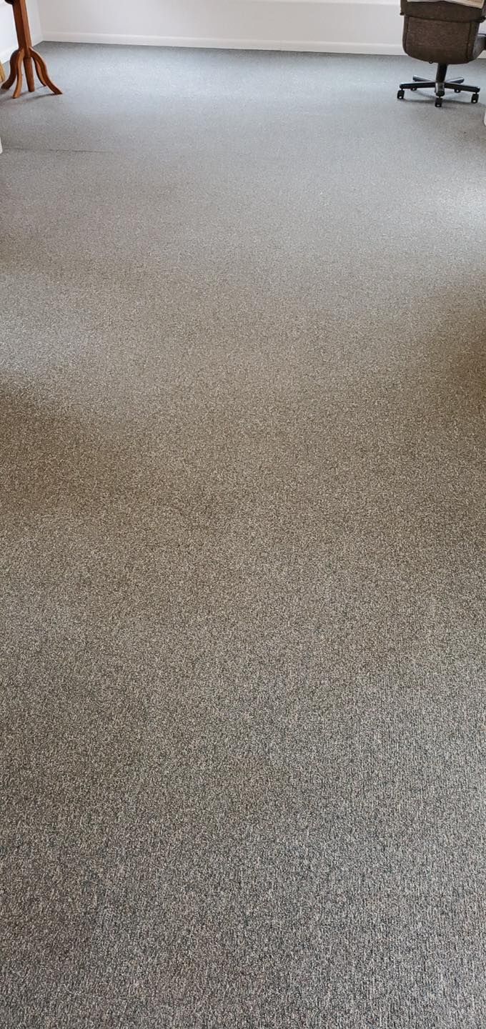 A room with gray speckled carpet, a white wall, a brown table, and an office chair.