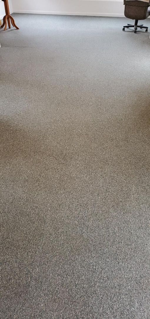 A room with gray speckled carpet, a white wall, a brown table, and an office chair.