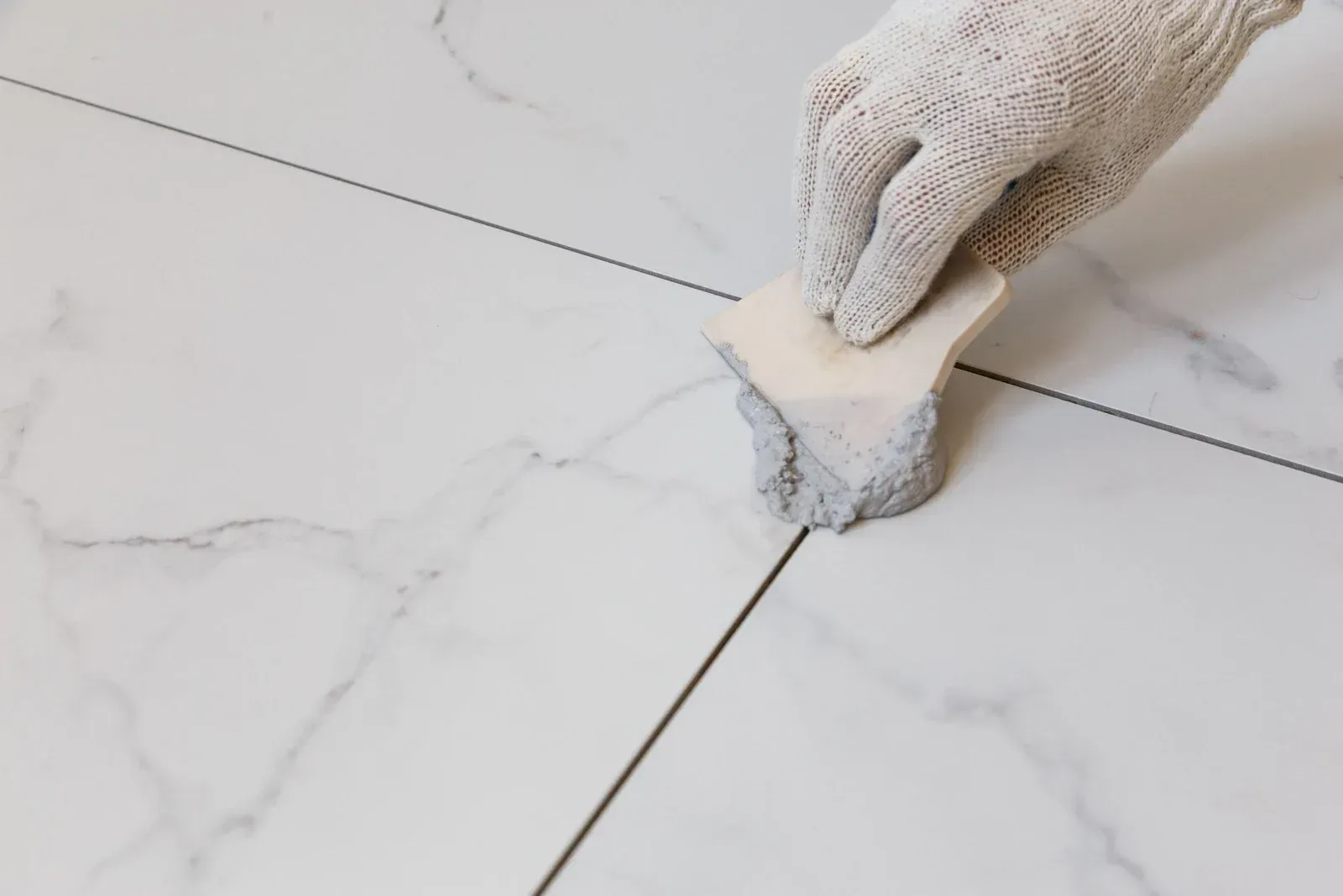 Gloved hand using a sponge to clean excess grout from white marble tile, black grout lines.