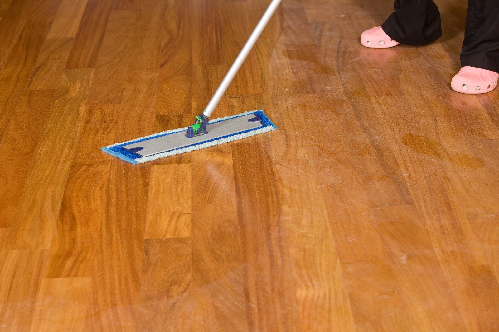 Person mopping a hardwood floor with a blue and silver mop, wearing pink slippers.