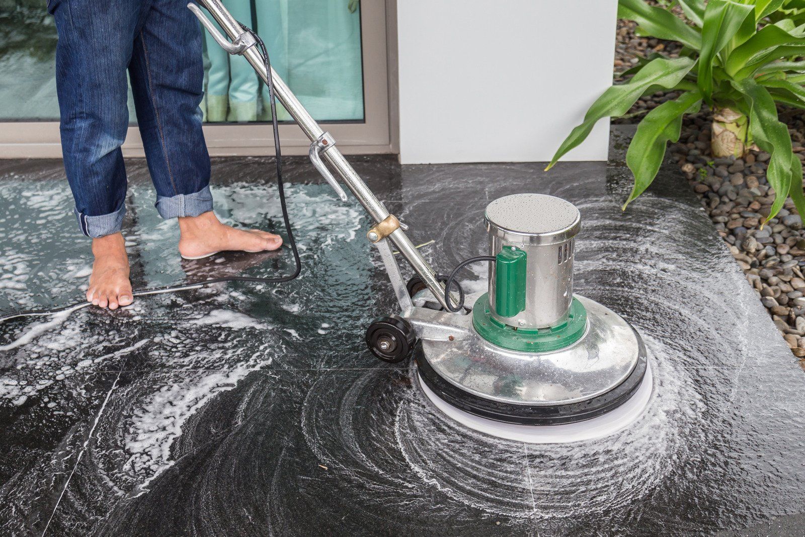 Person using a floor cleaning machine on a dark surface; outdoors.