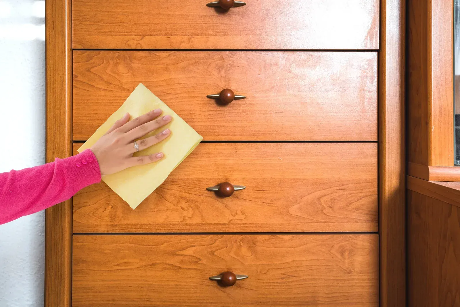 Person wiping a wooden dresser with a yellow cloth.