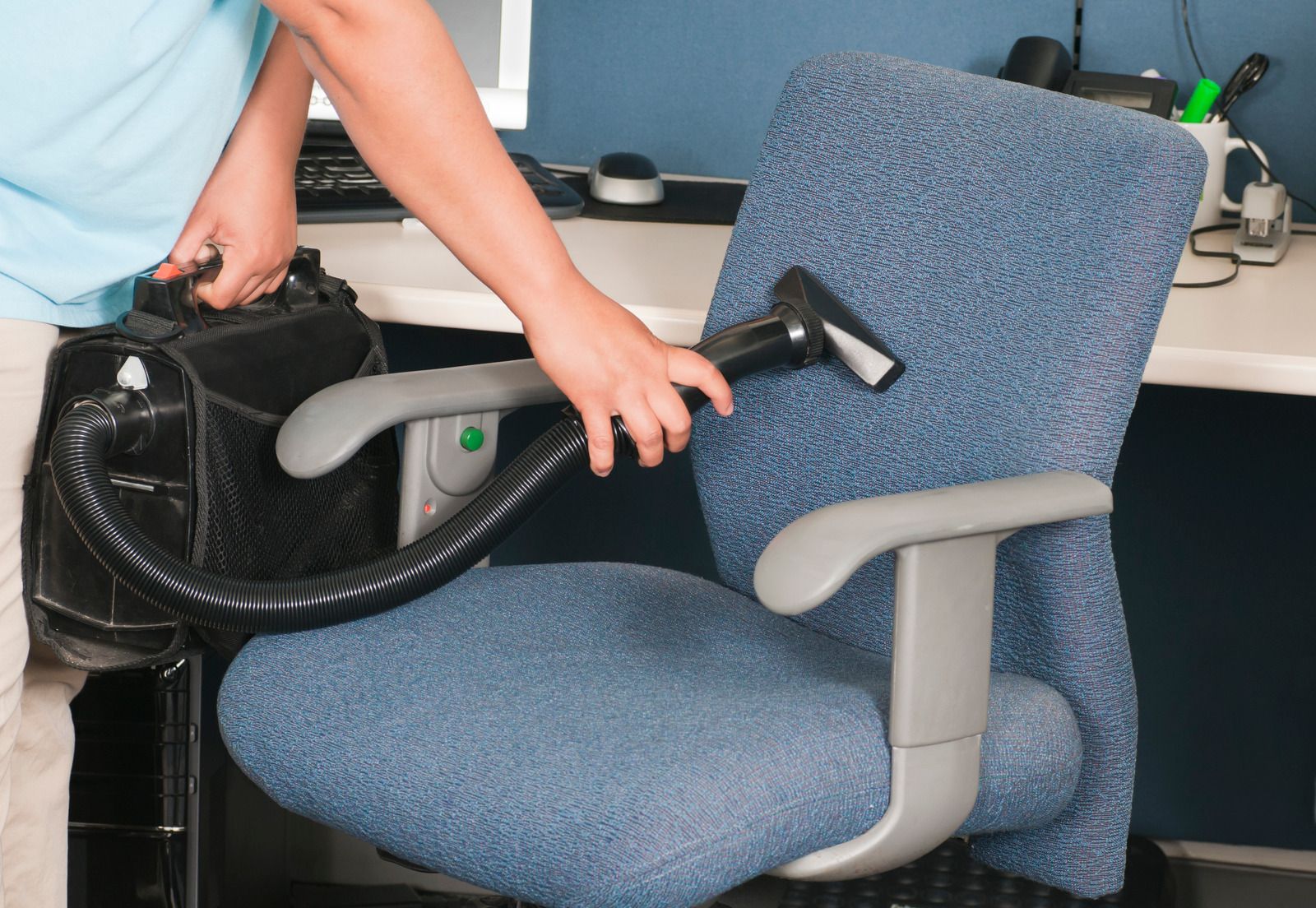 Person vacuuming a blue office chair with a backpack vacuum.