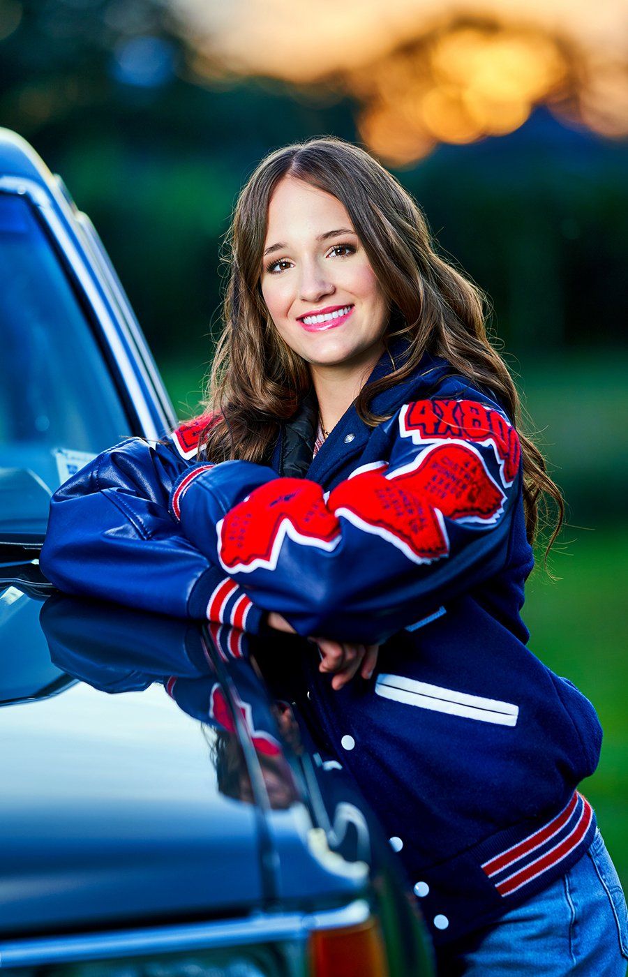 A woman in a blue and red jacket is standing next to a car.