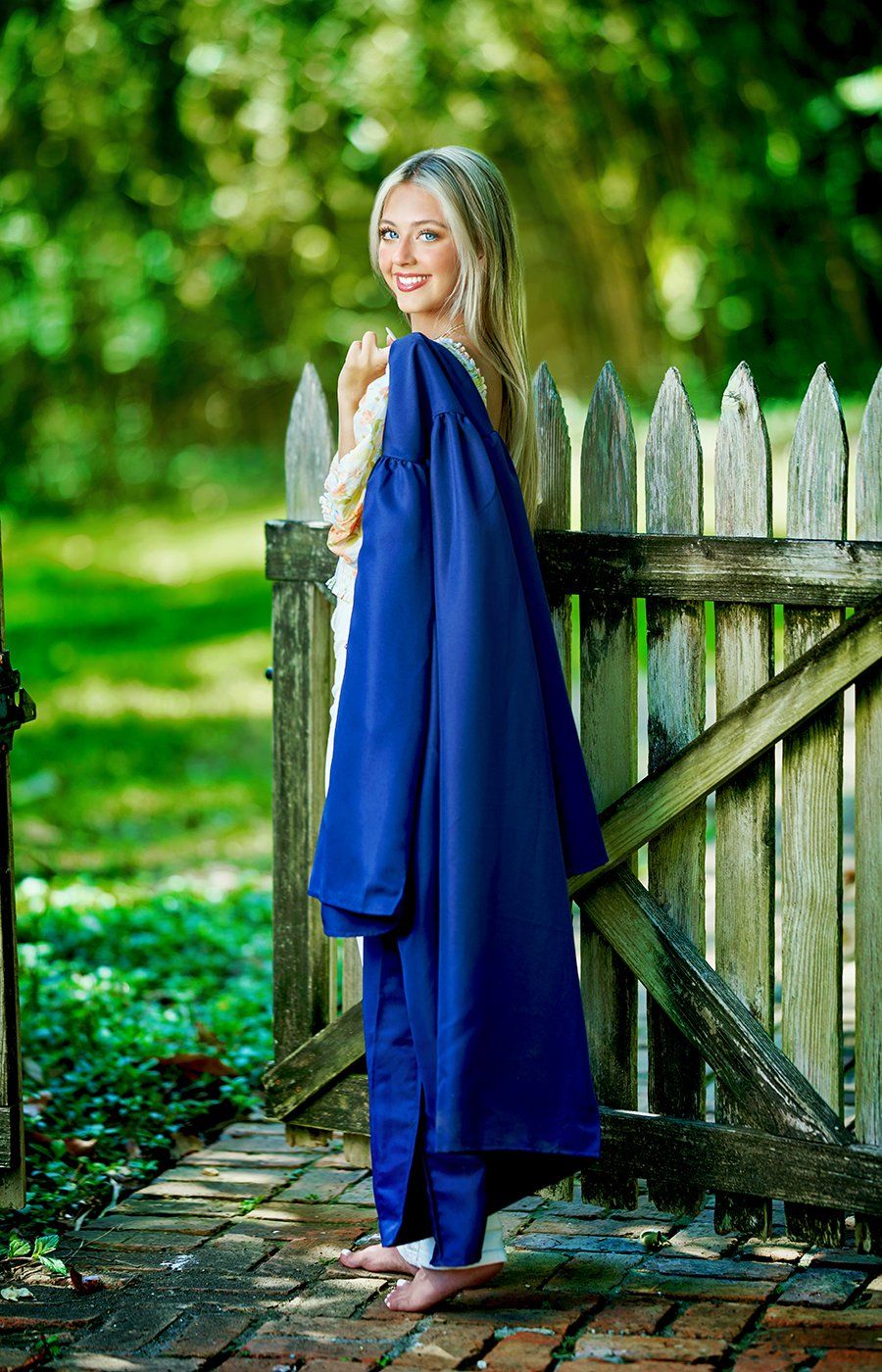 A woman in a blue cap and gown is standing next to a wooden fence.