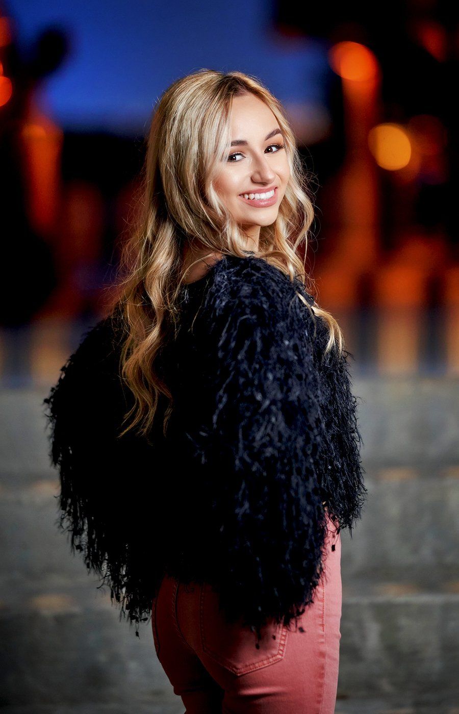 A woman is wearing a black fur jacket and pink pants.