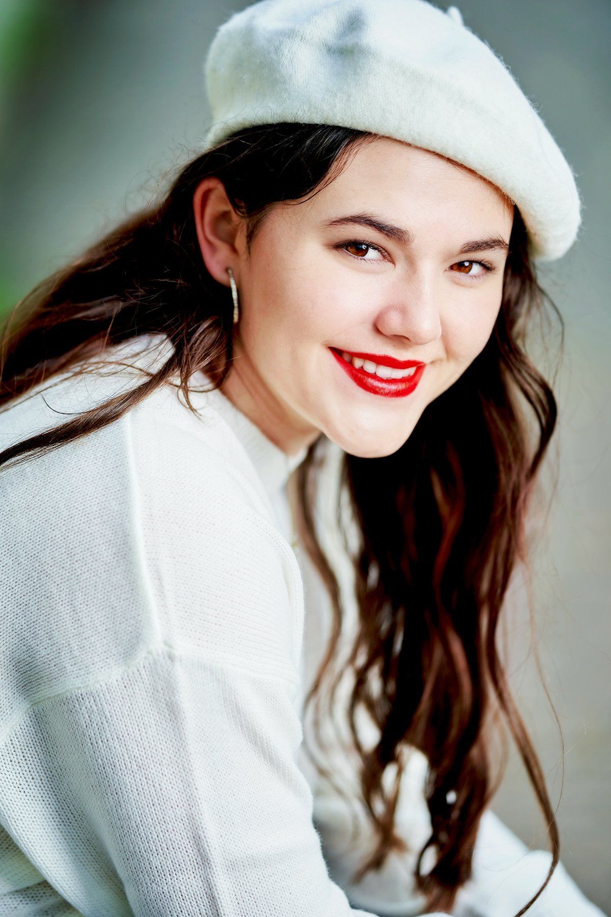 A woman wearing a white beret and red lipstick is smiling.