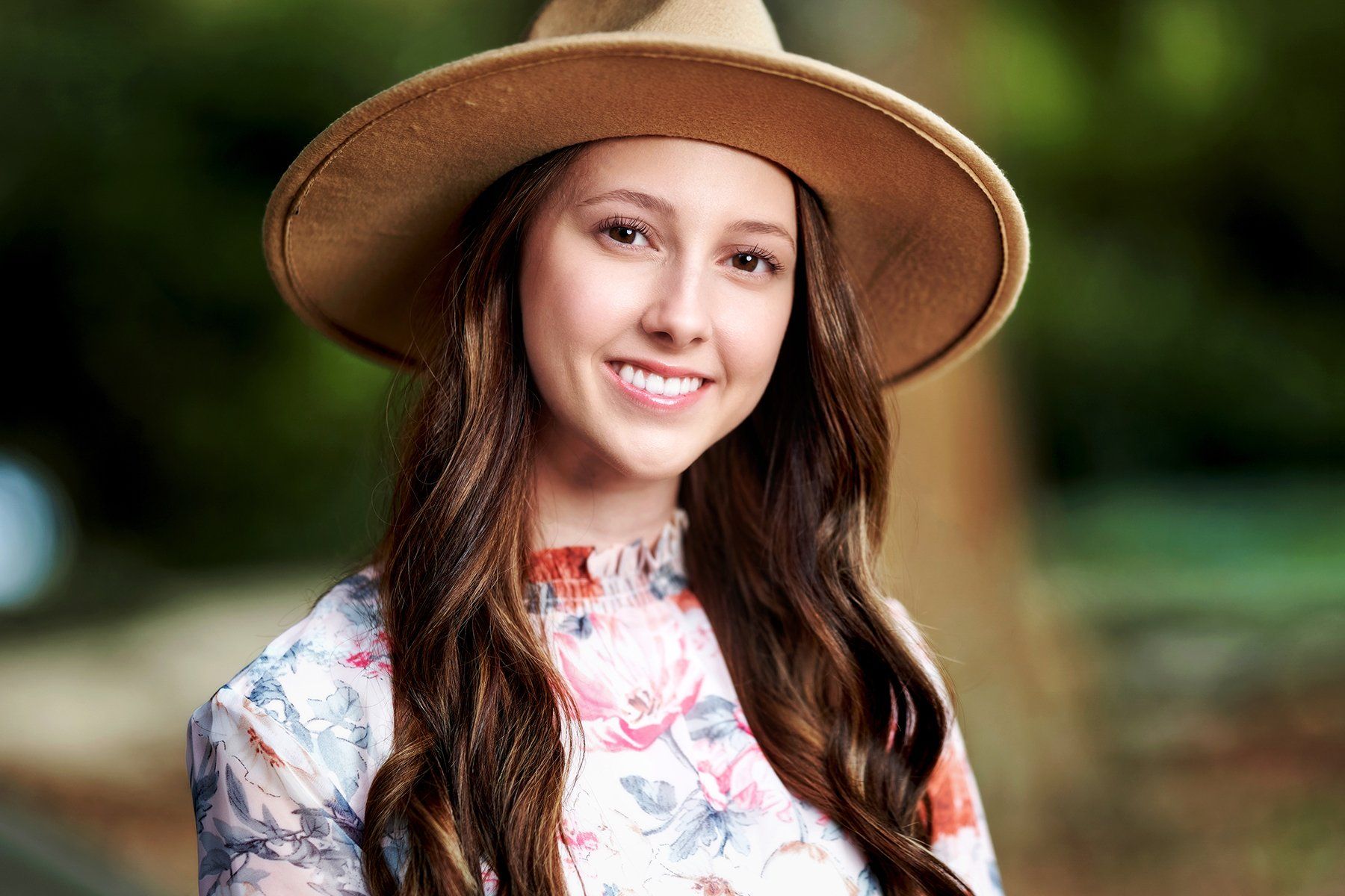 A young woman wearing a hat and a floral dress is smiling for the camera.