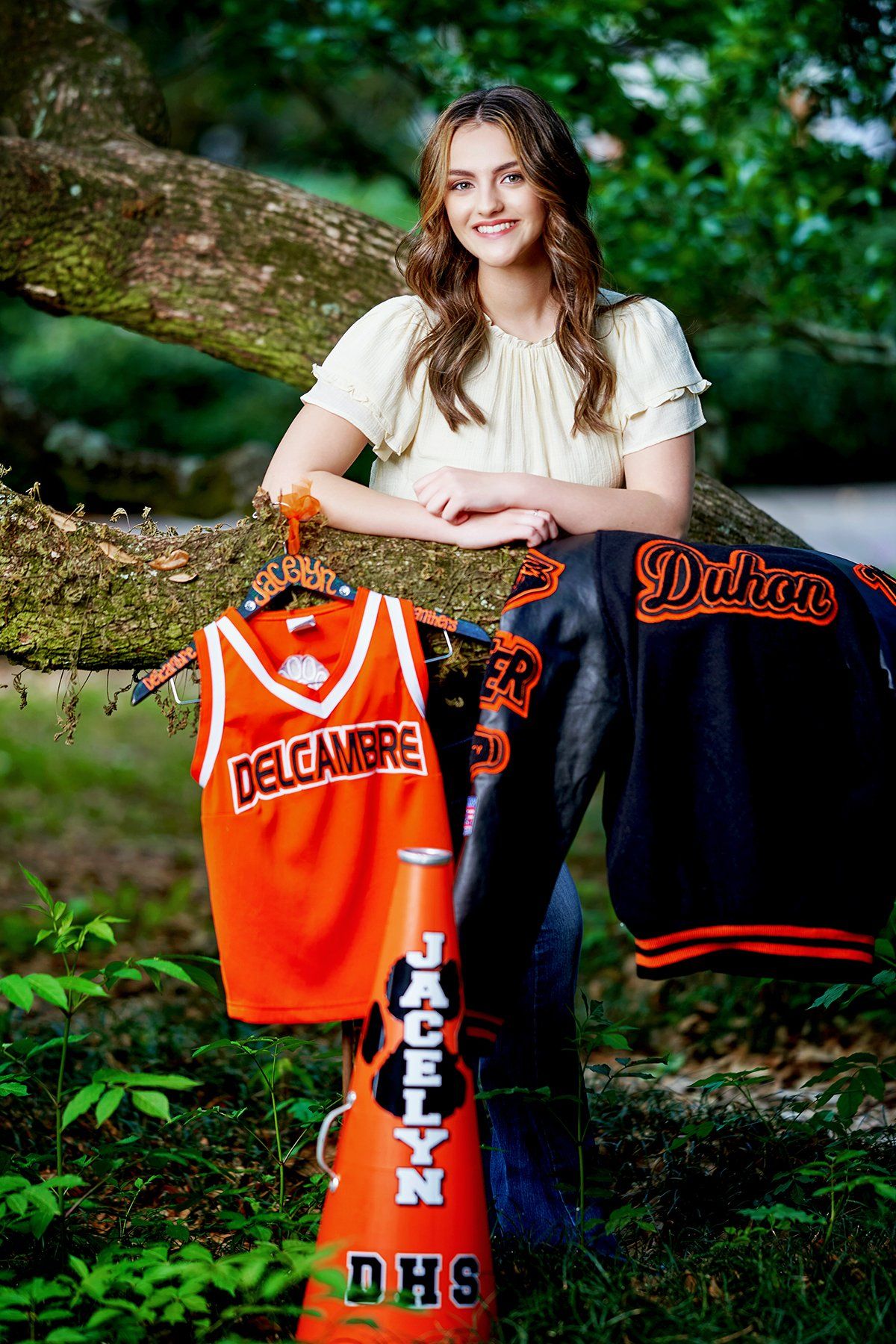 A woman is standing next to a tree holding a jersey and a cheerleader 's megaphone.