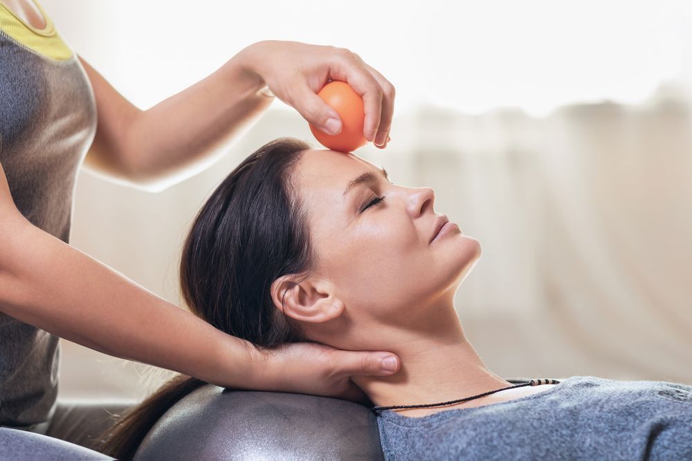 A woman is getting a massage with an orange ball on her forehead.