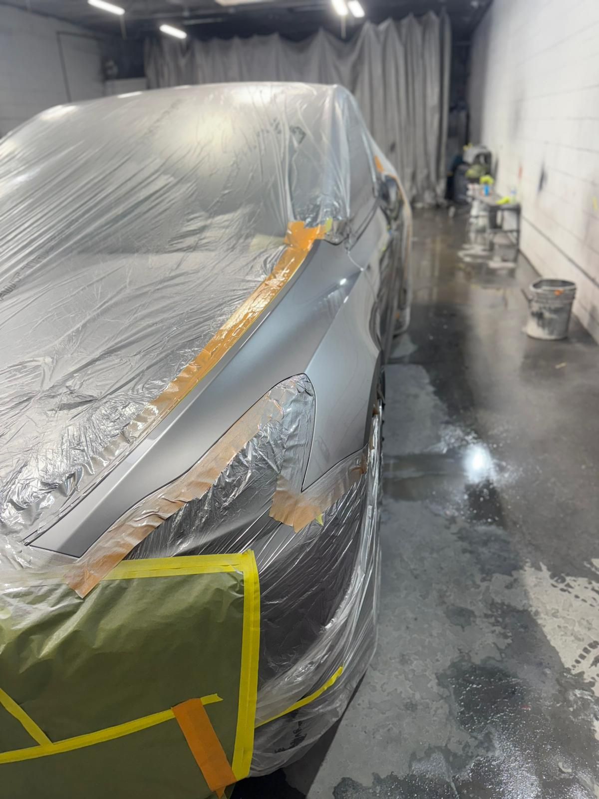 Car in a body shop, partially covered in plastic and taped off for painting.