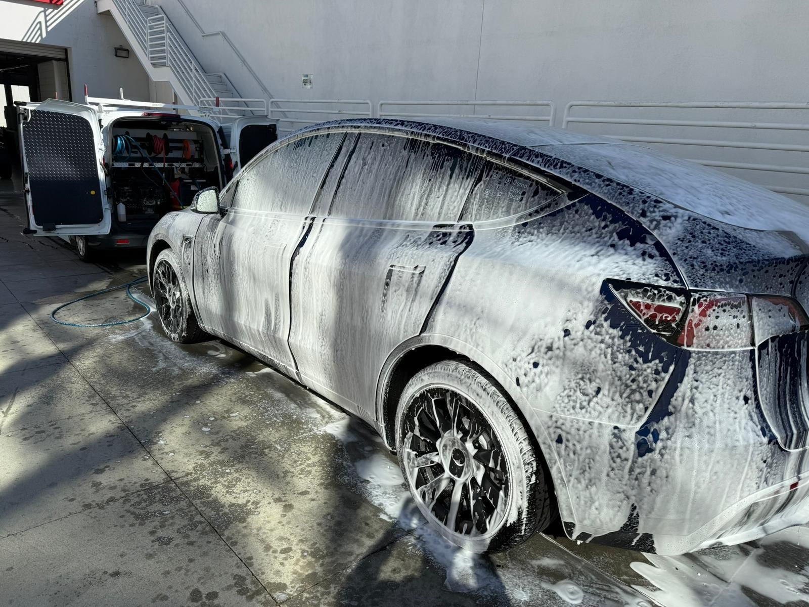 Tesla car covered in soap foam, being washed near a service van, exterior setting.