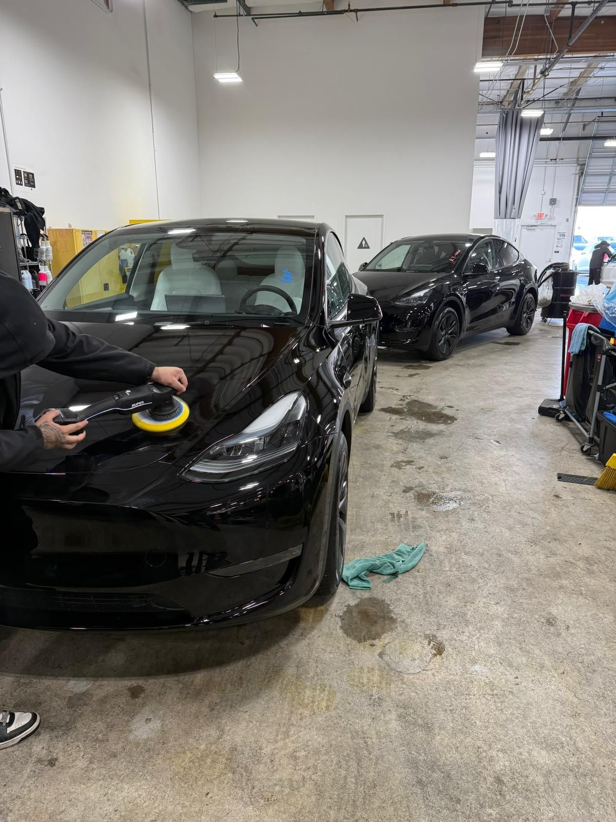 Person polishing a black Tesla car in a garage with another black Tesla parked in the background.