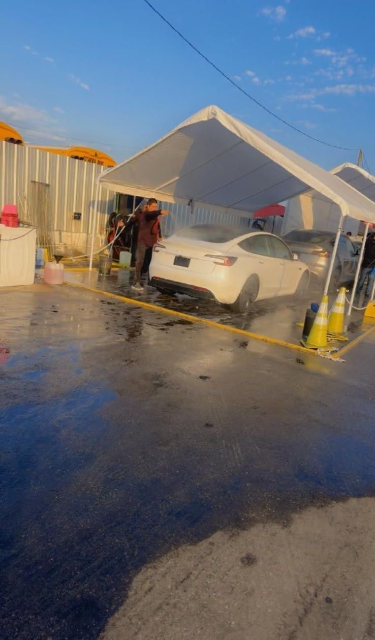 A person washing a white car under a white canopy at a car wash.