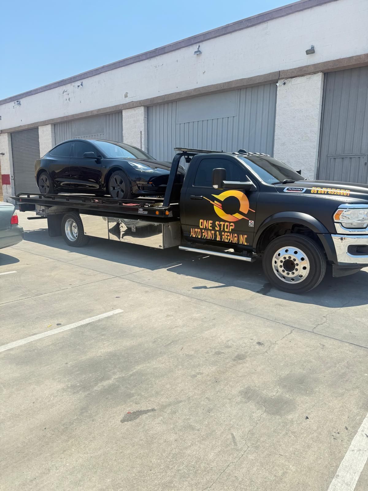 Black car on a flatbed tow truck in front of a building with white garage doors.