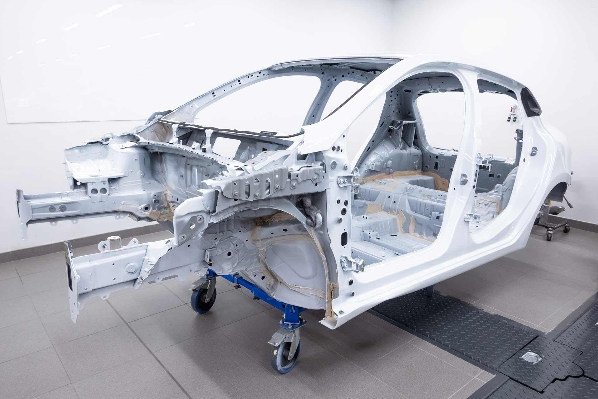 White car frame on a wheeled platform in a studio.