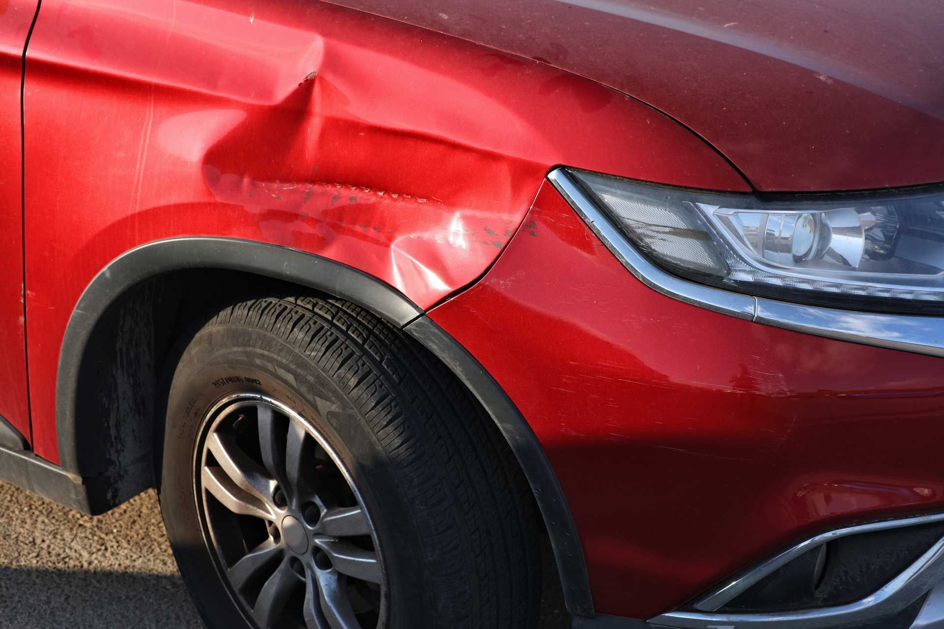 Red car with a dented front fender above the wheel.