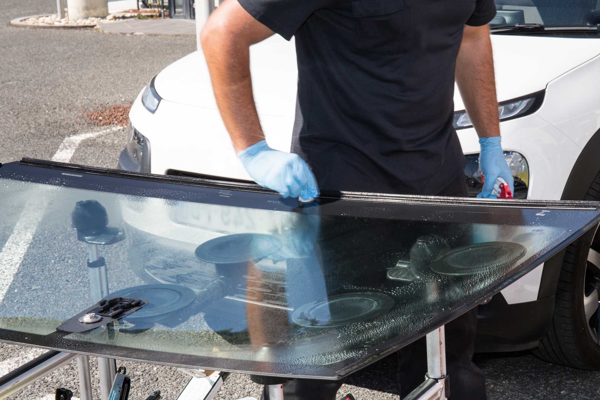 Person wearing gloves cleaning a car windshield, with a car in the background.