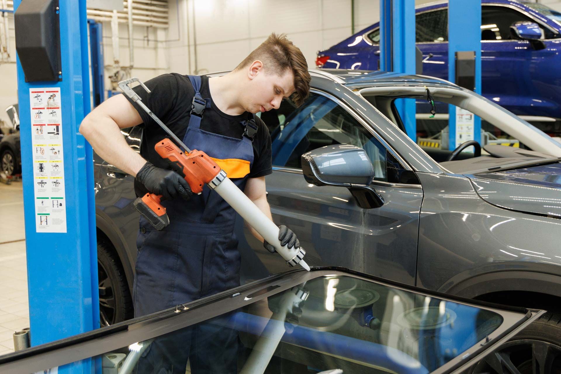 Mechanic applying sealant to a car windshield in a repair shop.