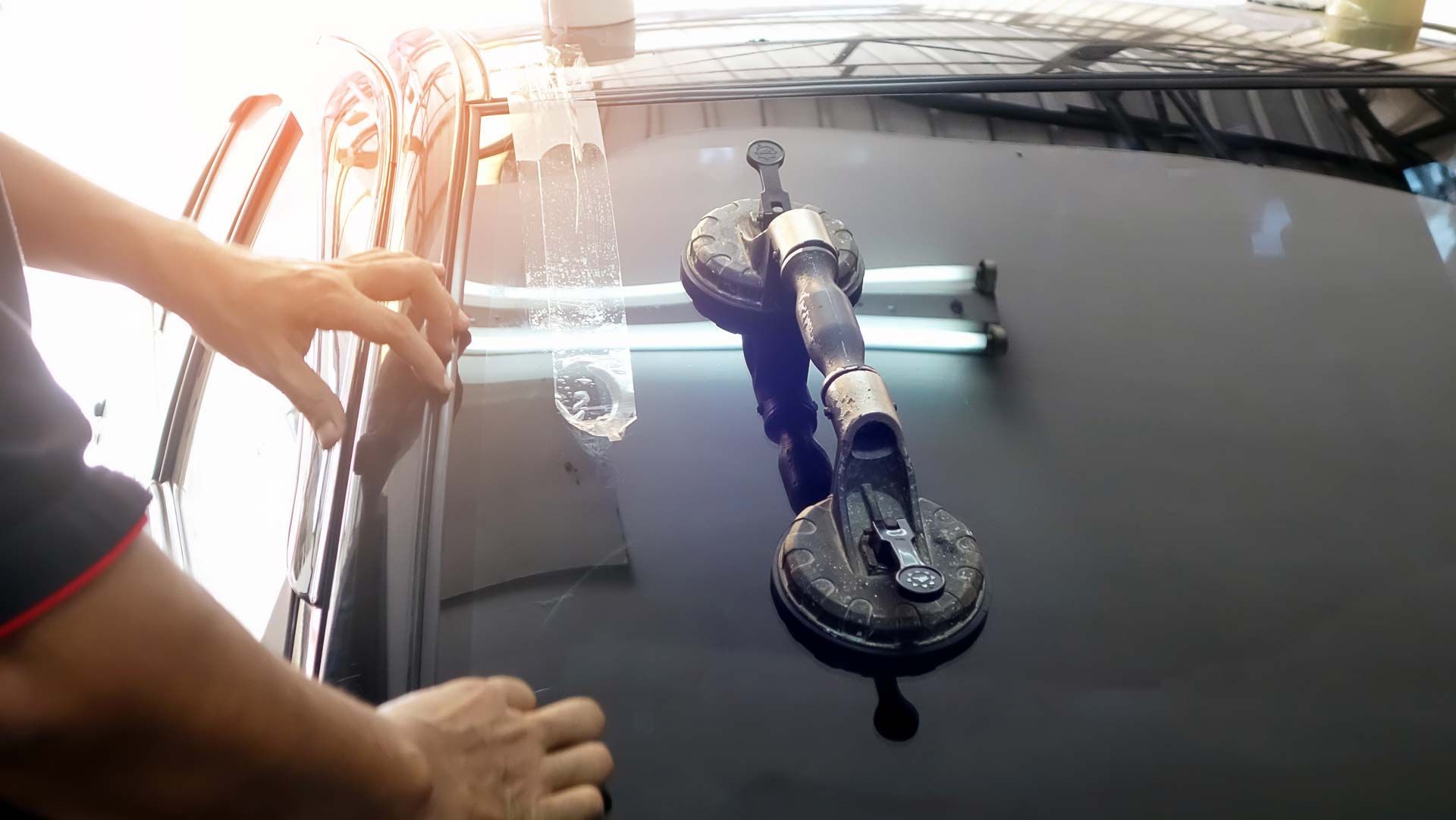 Person using a suction cup tool to lift a car windshield.