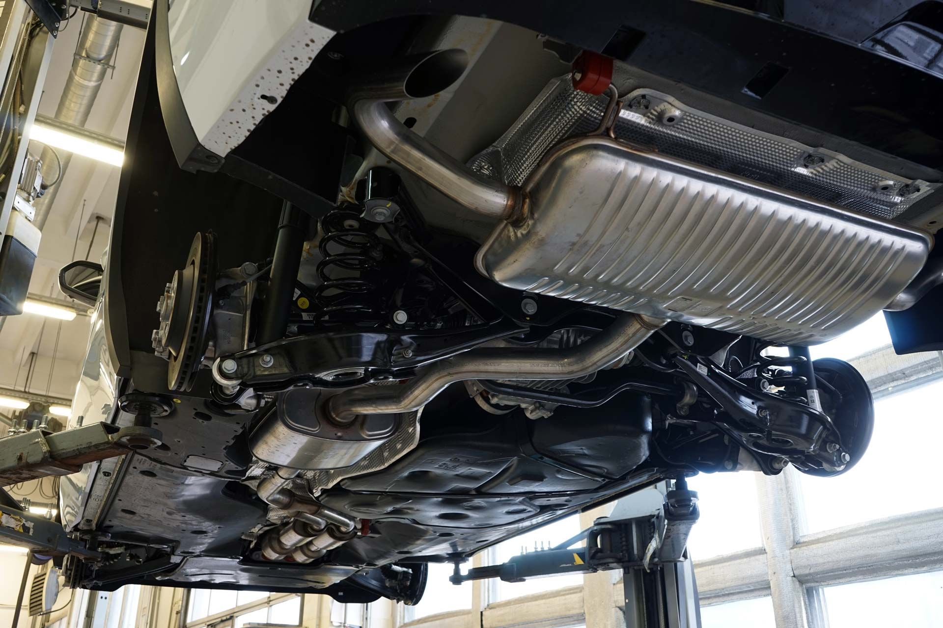 Undercarriage of a car on a lift; silver exhaust system and other mechanical components visible.