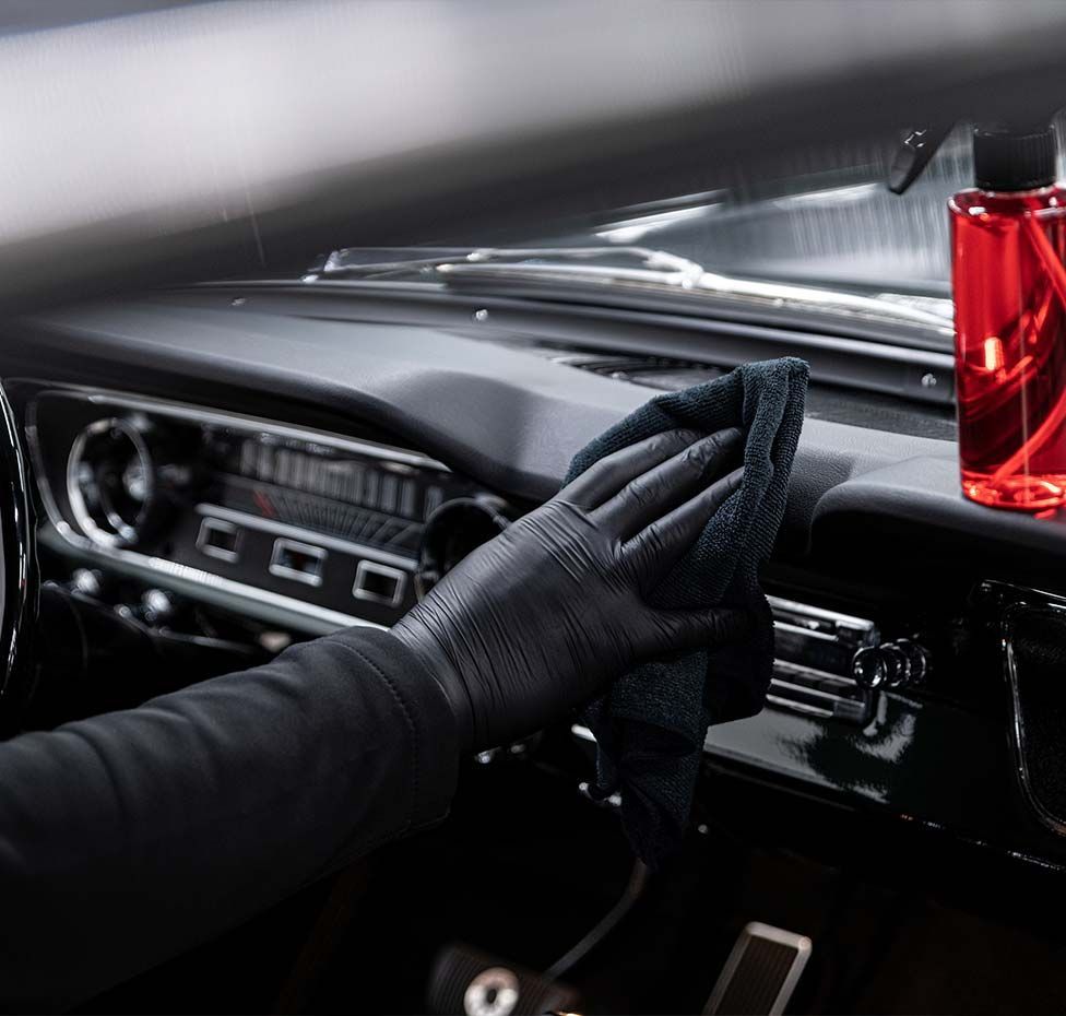 Person wearing black gloves cleaning a car dashboard with a cloth.