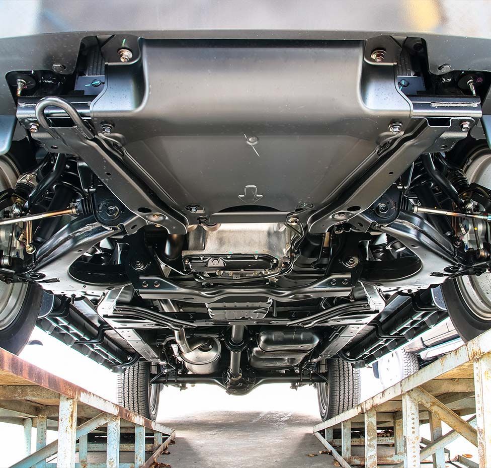 Underside of a car on a lift; shows axles, suspension, and exhaust components, painted black.