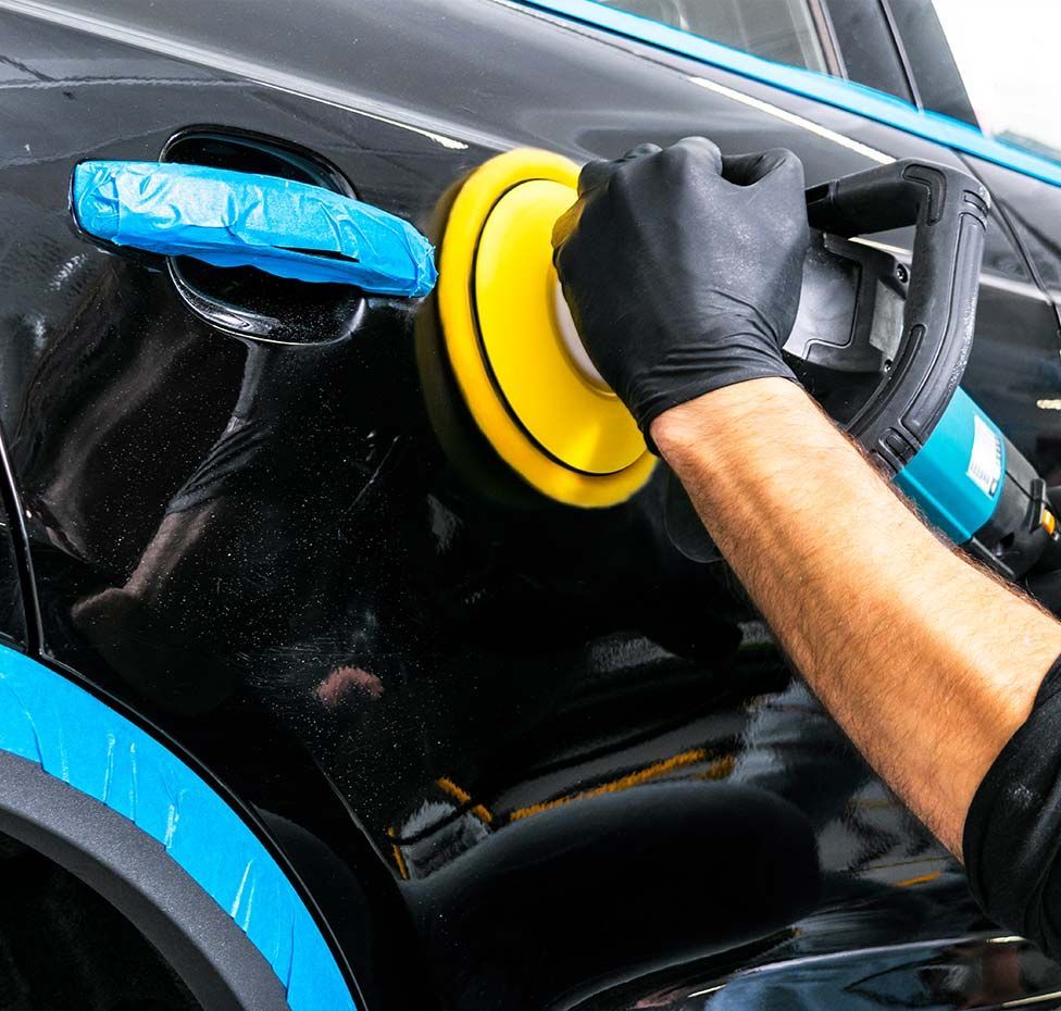 Person polishing a black car with an electric polisher; close-up view.