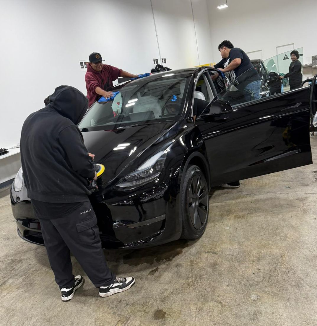 Three people cleaning a black Tesla.