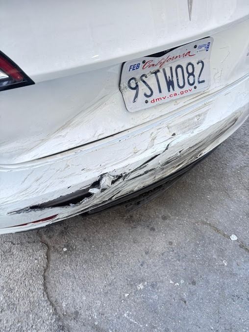 White Tesla's rear bumper damaged with dents, cracks, and license plate.