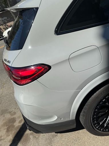 Rear quarter panel of a white Mercedes-Benz AMG SUV, black rim, taillight, gas cap door.