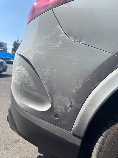 Damaged white car bumper with scratches and dents.