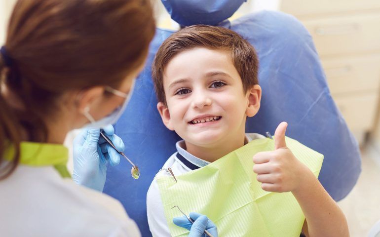 A young boy is giving a thumbs up while sitting in a dental chair.