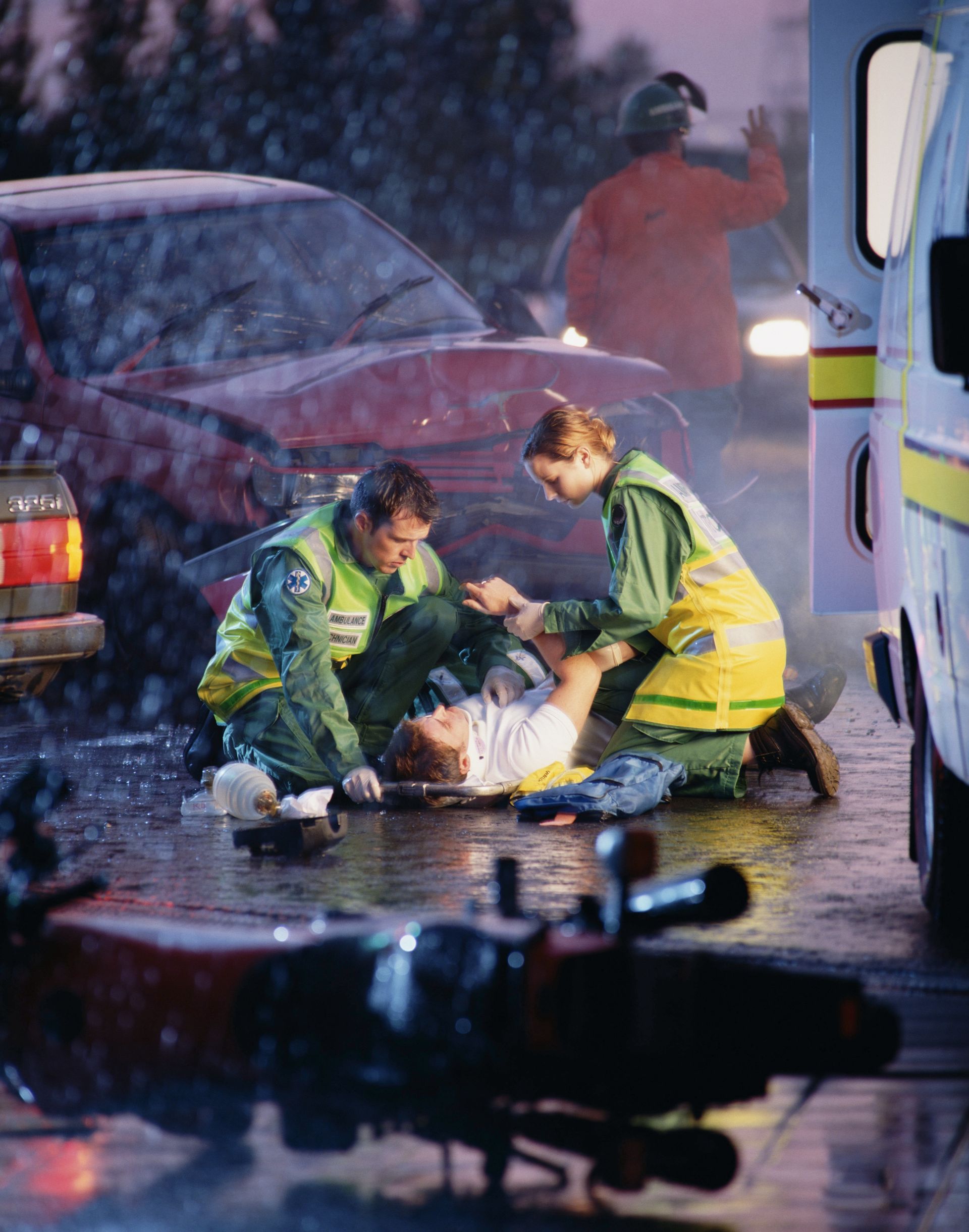 Emergency responders attending to injured person at car accident scene.