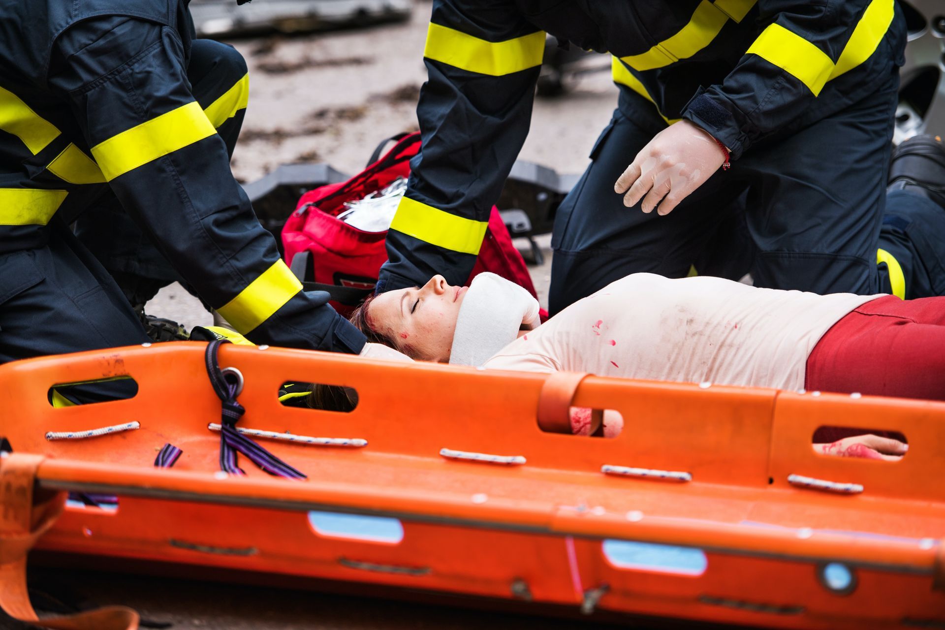 Emergency responders tending to a person on a stretcher after an accident; bandaged head, blood visible.