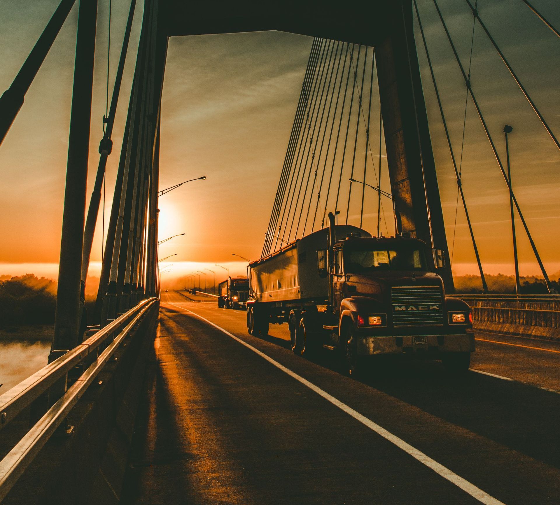 Semi-truck driving over a bridge at sunset.