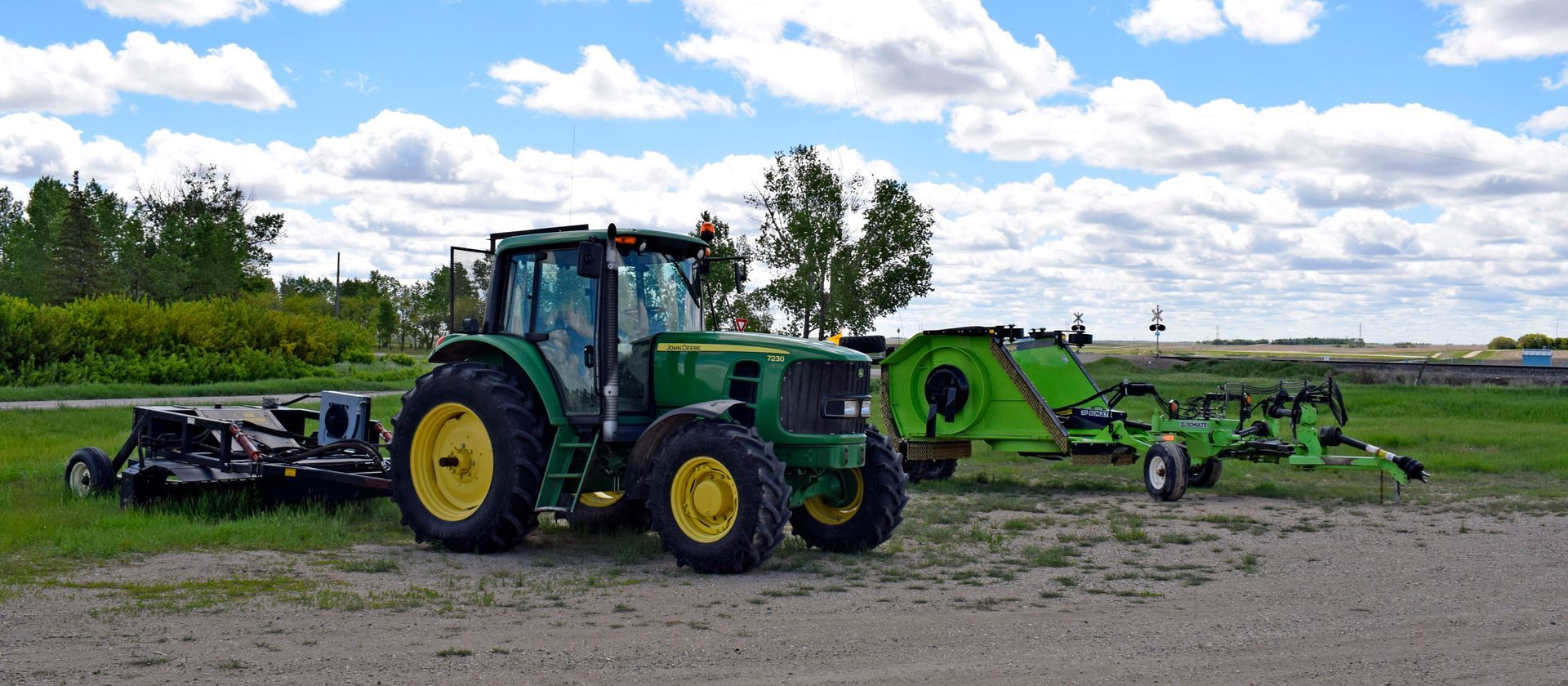 A green tractor is parked in a grassy field with a trailer attached to it.