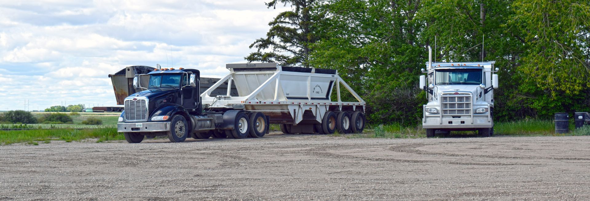 Two dump trucks are parked next to each other on a gravel road.