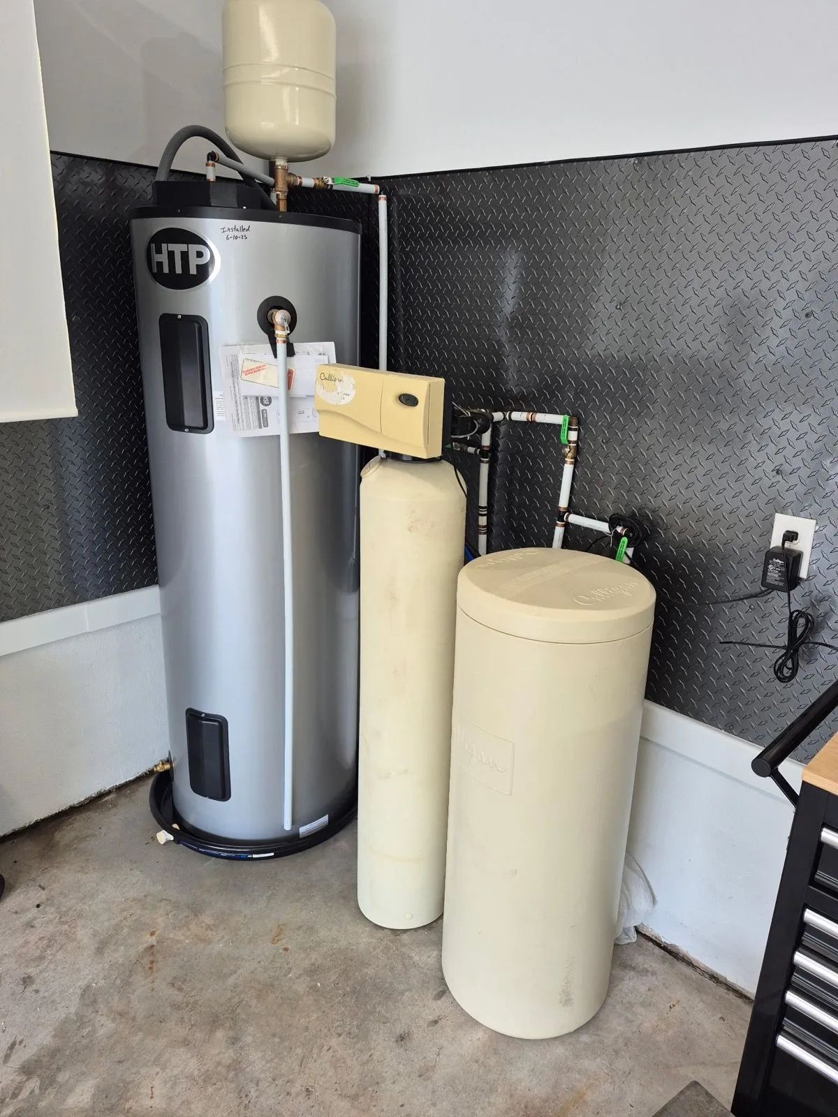 Water heater with attached filtration tanks in a utility room corner.