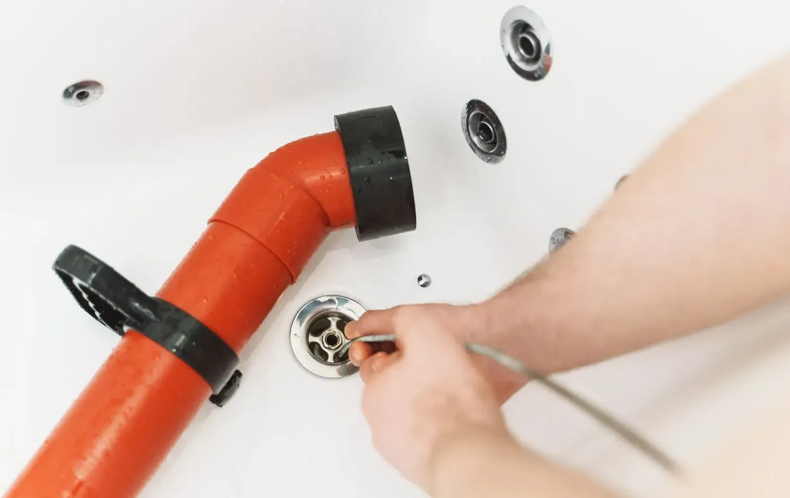 Hand tightening a bathtub drain around a red pipe in a white tub