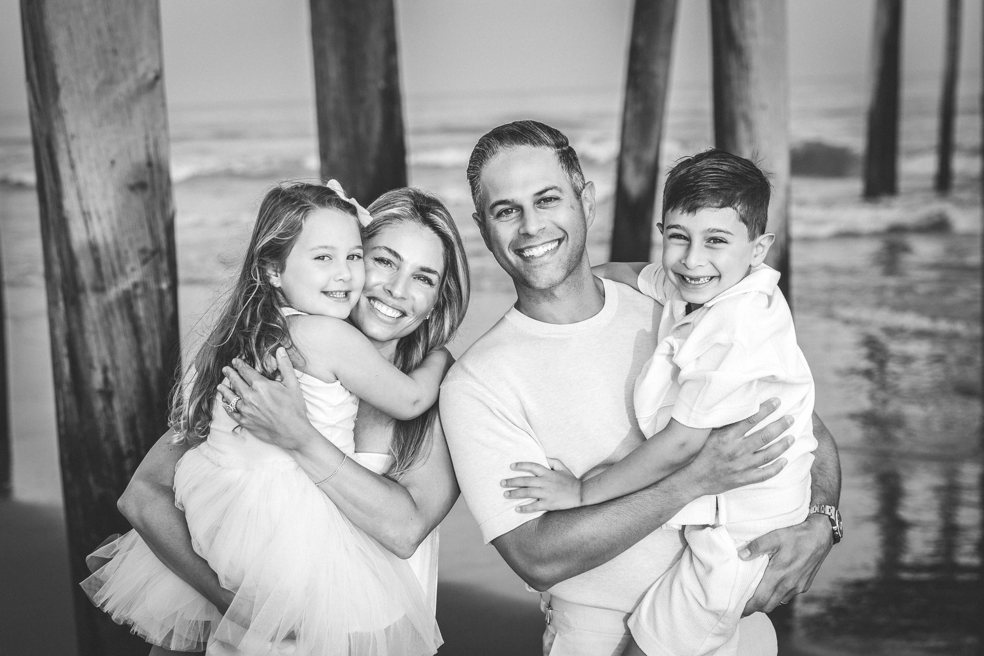 Black-and-white family photo of Dr. Cogan and Amber holding their two children on the beach