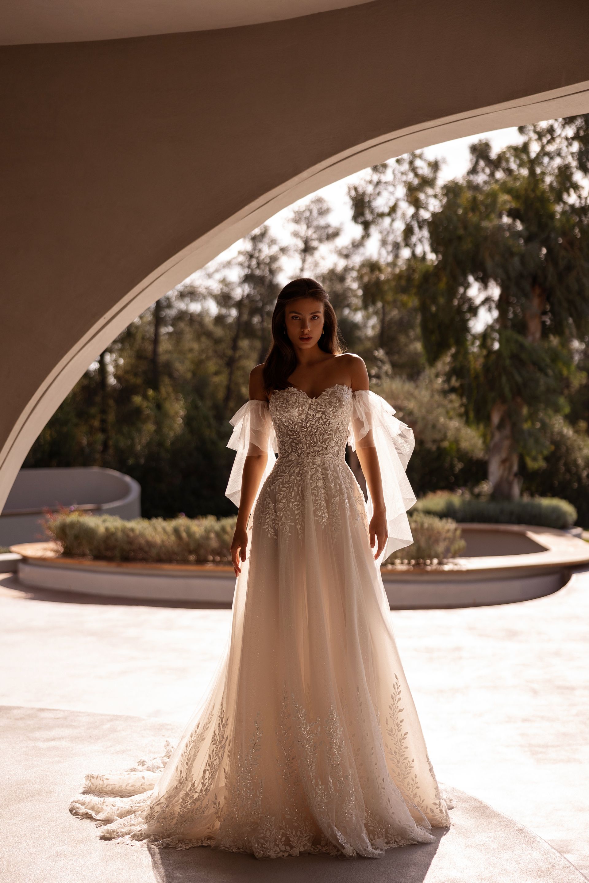 Una donna in un abito da sposa decorato con spalle scoperte è in piedi davanti a un portone ad arco